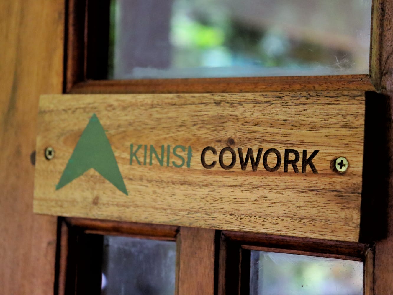 A carved wooden Kinisi Cowork nameplate mounted on the door frame.