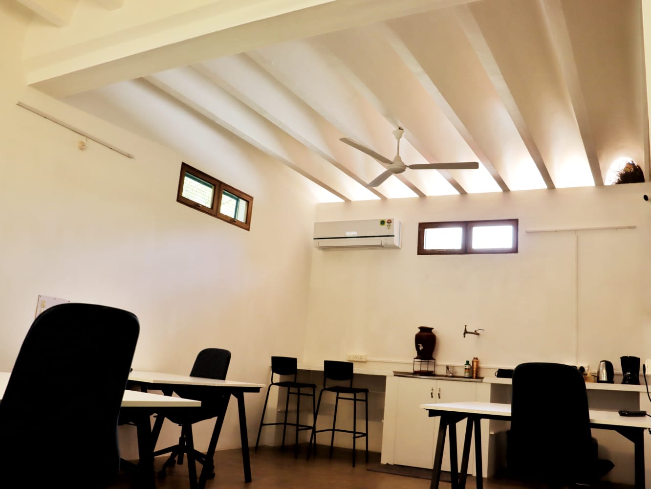 A workroom with a high beamed ceiling, ceiling fan, air conditioner and a pantry counter.