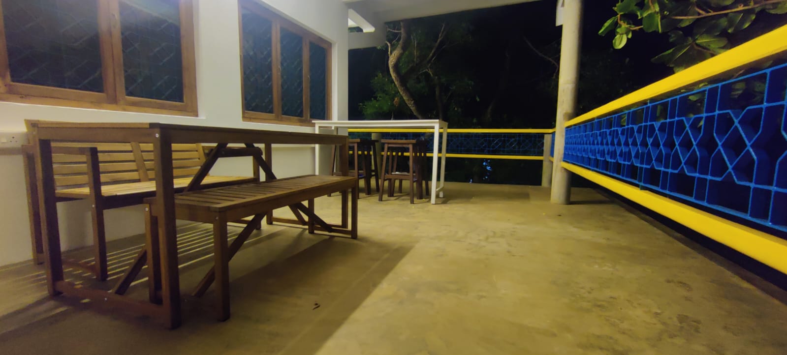 The outside seating at Kinisi Cowork: wooden benches and a high table on the veranda, under the trees.